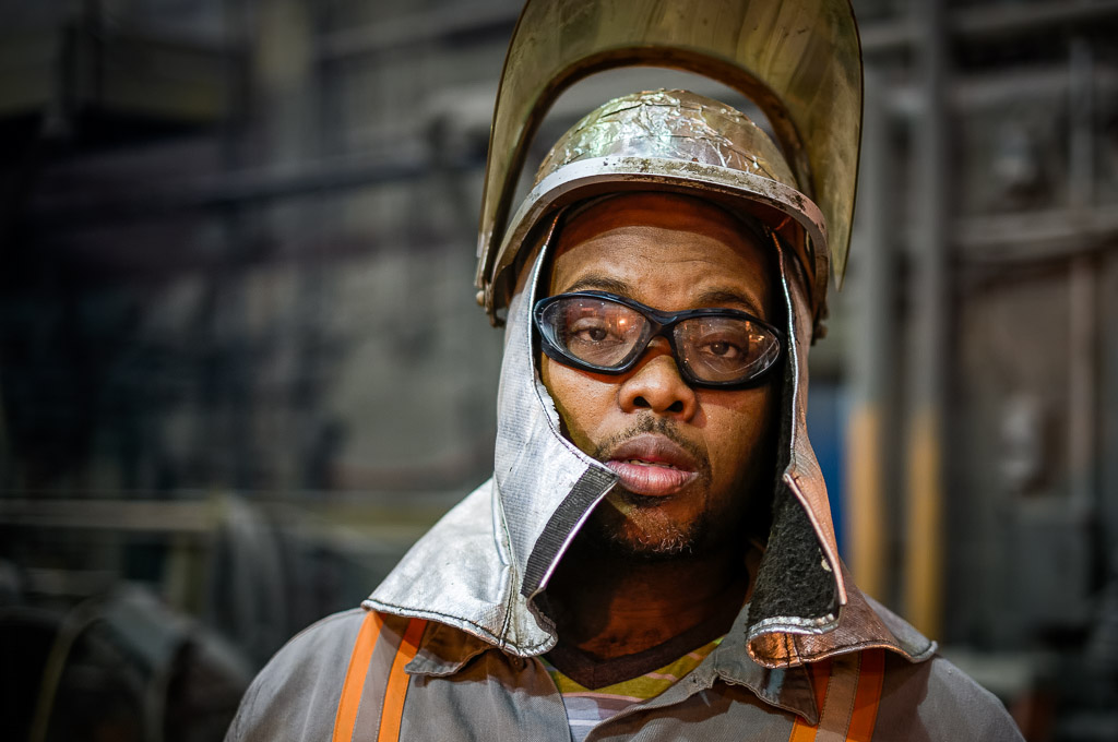 An operations tech in a cooler moment.  Note the aluminum foil heat-reflecting wrap on the helmet.  Although you have a suit, snook (the head covering you can see), gloves and so forth, if you were to spend much time near the really hot stuff your hard hat will start to burn and get pretty hot.

Please like my Facebook Artists page: <a href=